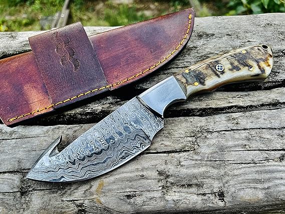 Damascus steel gut hook skinning knife with ram horn handle and leather sheath, 9 inches overall