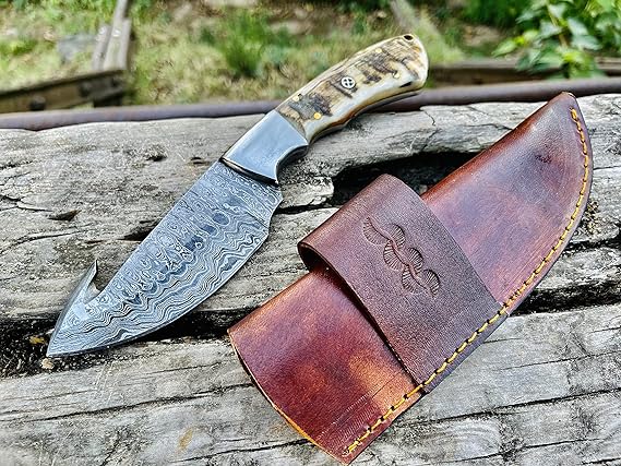 Damascus steel gut hook skinning knife with ram horn handle and leather sheath, 9 inches overall