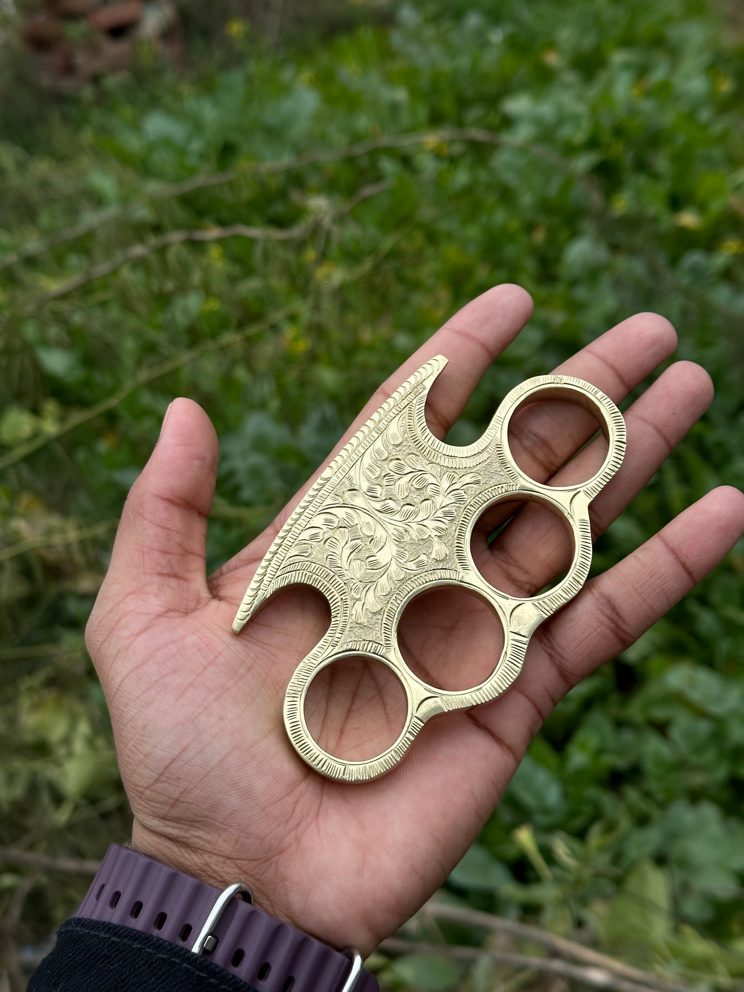 Brass knuckle duster with intricate engraving, paired with a leather case for everyday carry