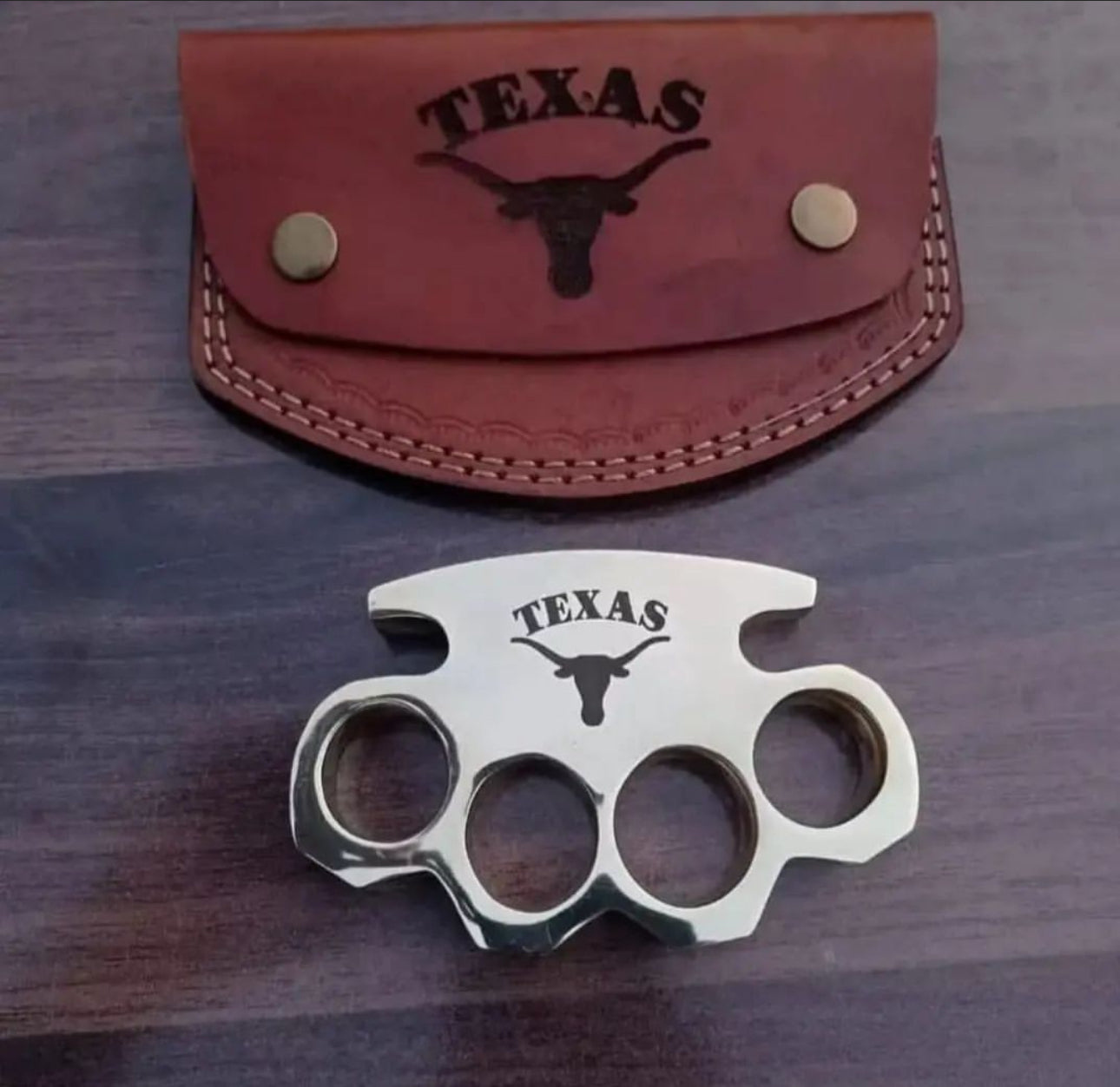 Brass knuckle with engraved design displayed alongside a leather belt loop case