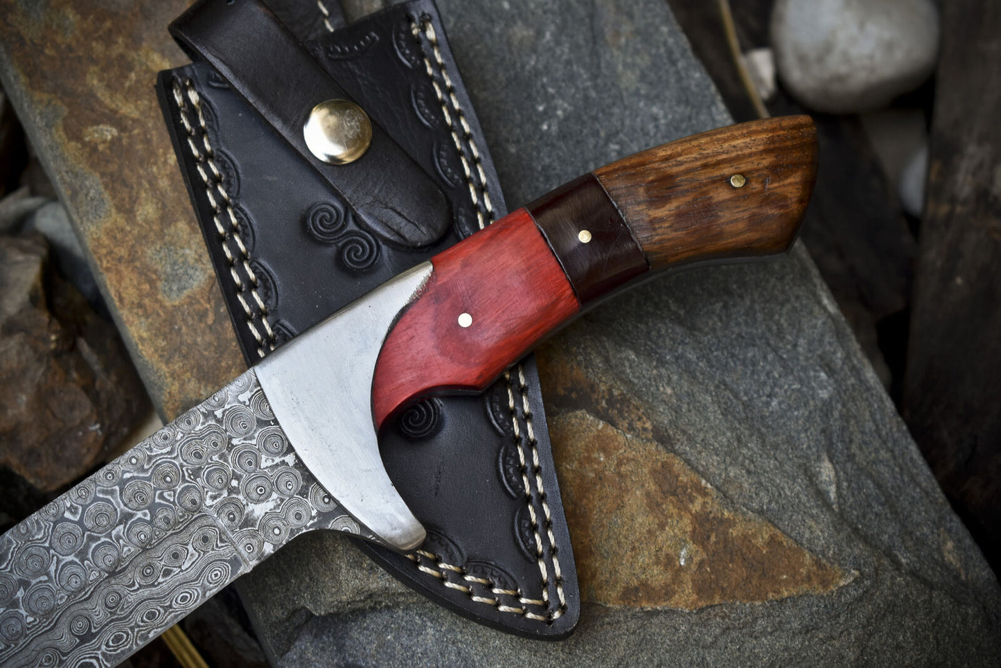Close-up of Damascus steel hunting knife with pakkawood and rosewood handle, featuring leather sheath