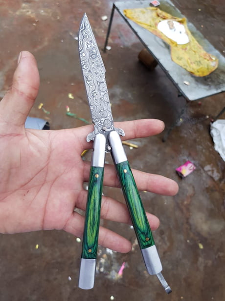 Damascus butterfly knife featuring a drop-point blade and pakkawood handle, stored in a leather case