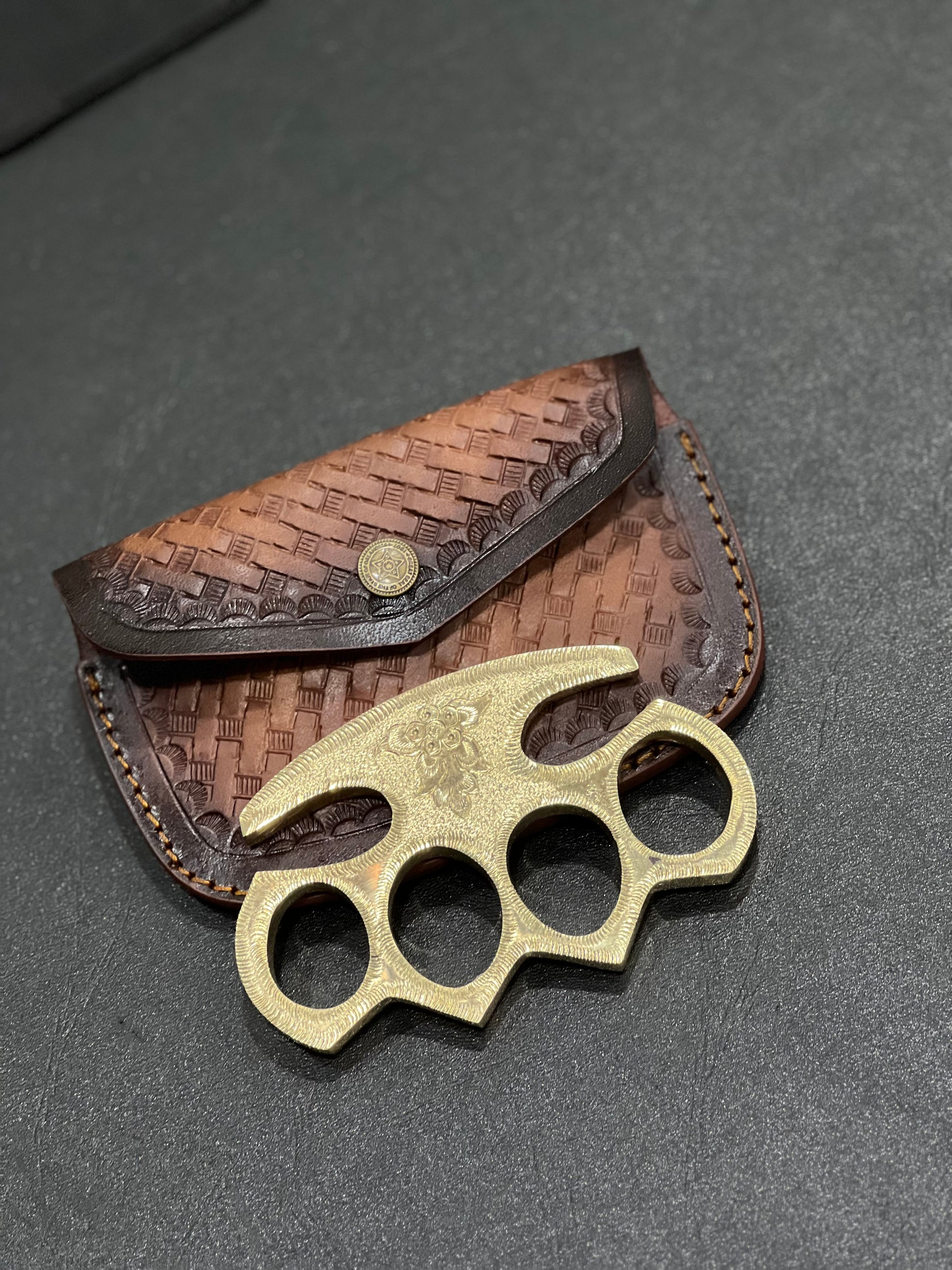 Engraved brass knuckles for self-defense and everyday carry, featuring a leather case.