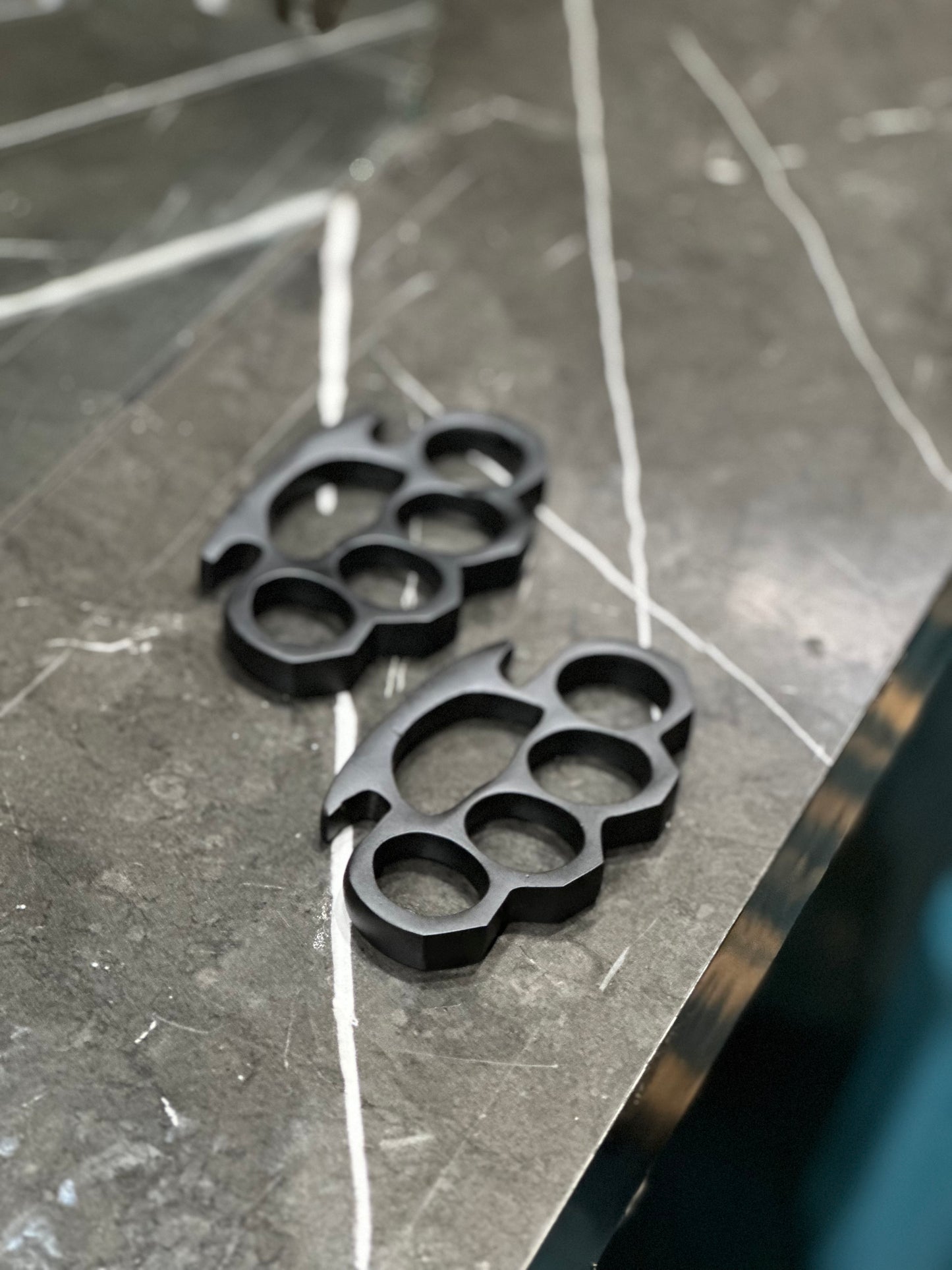 Handcrafted black steel knuckle duster with intricate engravings and solid brass material, complete with a leather case