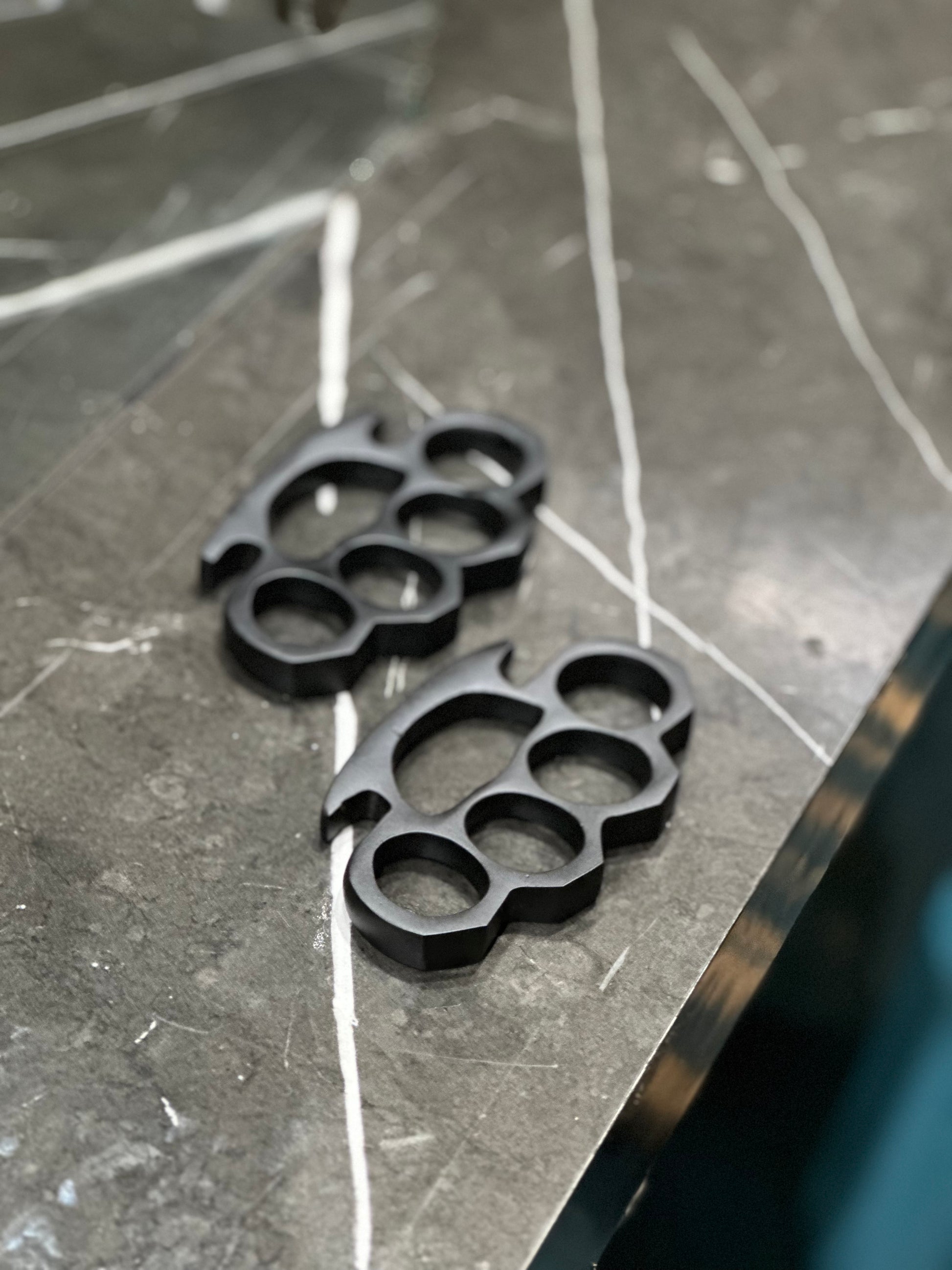 Handcrafted black steel knuckle duster with intricate engravings and solid brass material, complete with a leather case