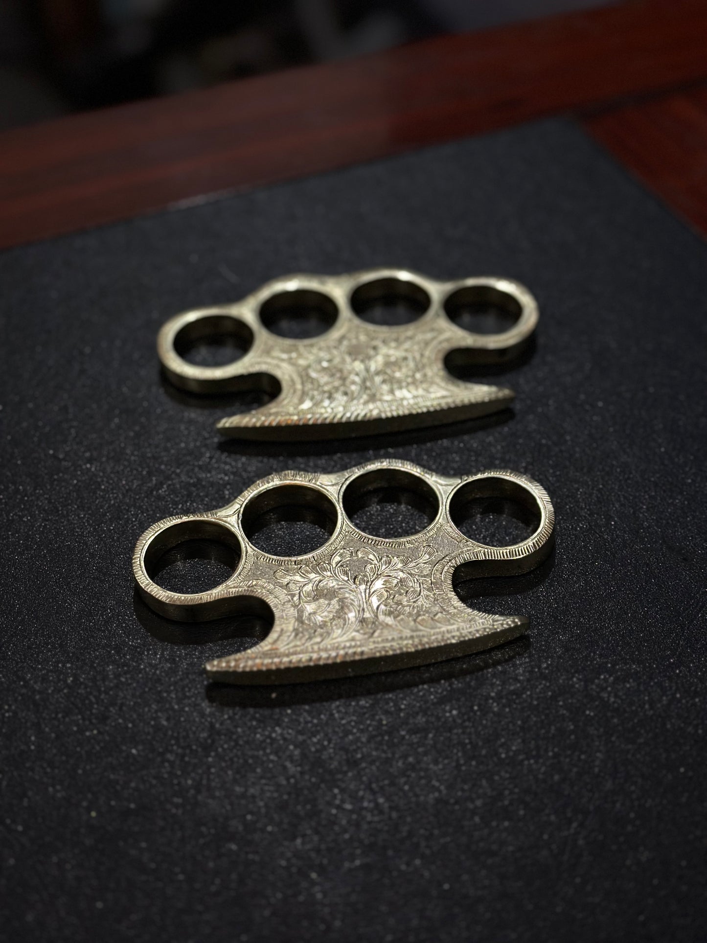 Solid brass knuckle duster with intricate engraving and leather belt loop case for everyday carry.