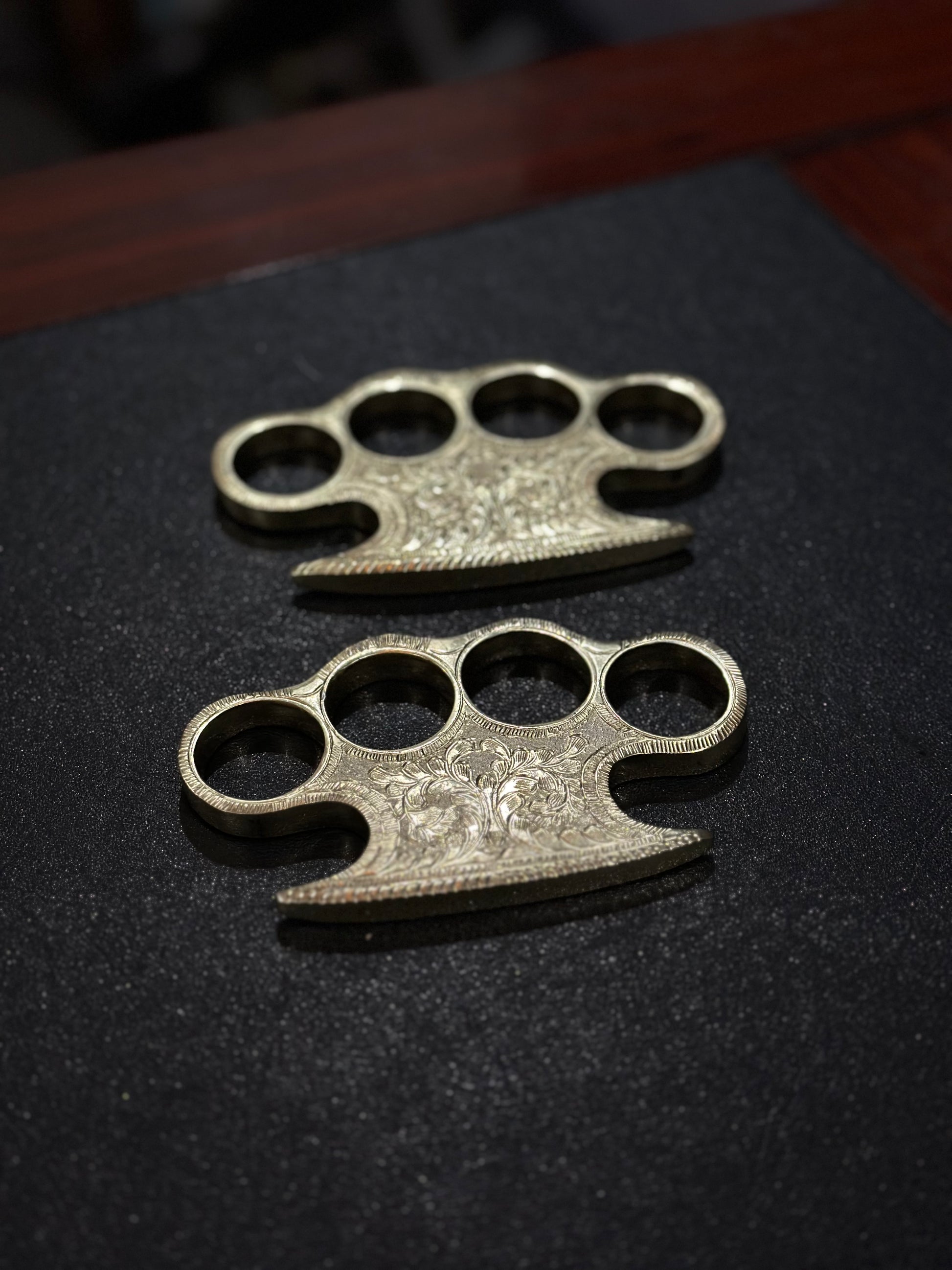 Solid brass knuckle duster with intricate engraving and leather belt loop case for everyday carry.