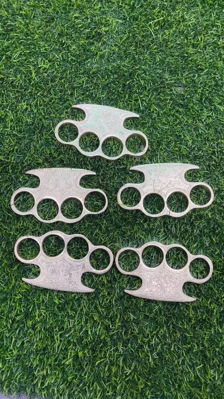 Solid brass knuckle featuring detailed custom engravings, displayed with a leather belt loop case