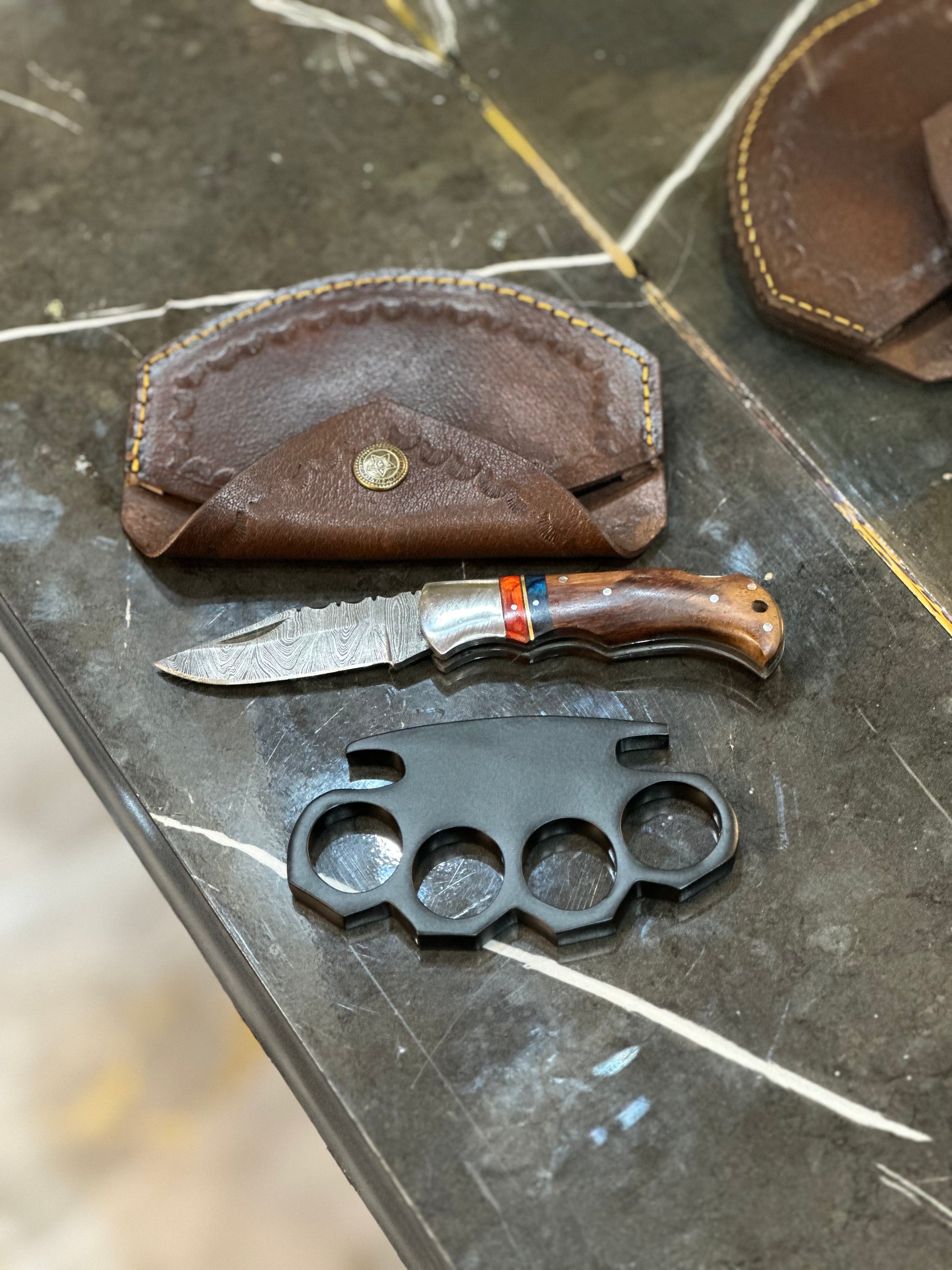 Black steel knuckle duster with custom engravings and a hidden pocket knife, featuring a solid brass build and leather case