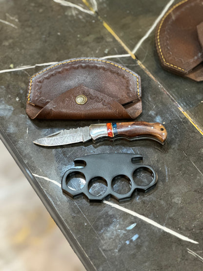 Black steel knuckle duster with custom engravings and a hidden pocket knife, featuring a solid brass build and leather case