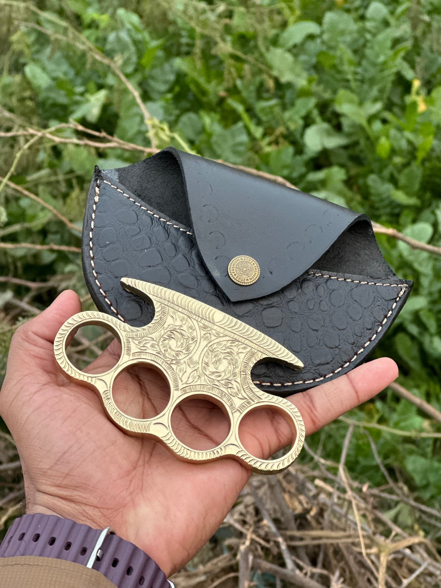 Close-up of custom engraved brass knuckle, showcasing detailed craftsmanship and leather belt loop case