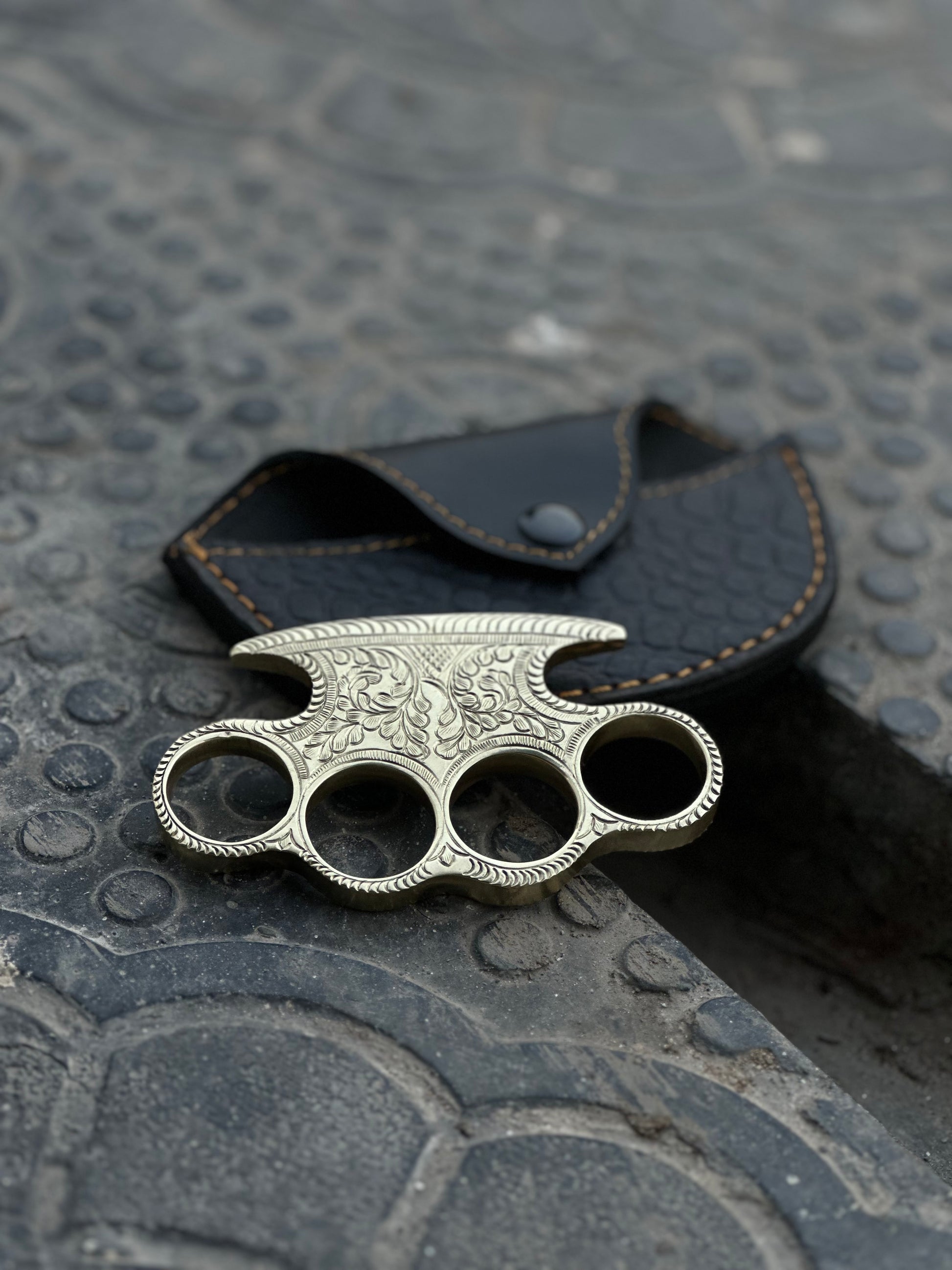 "Engraved brass knuckles in a belt loop leather case, perfect for collectors and self-defense."

