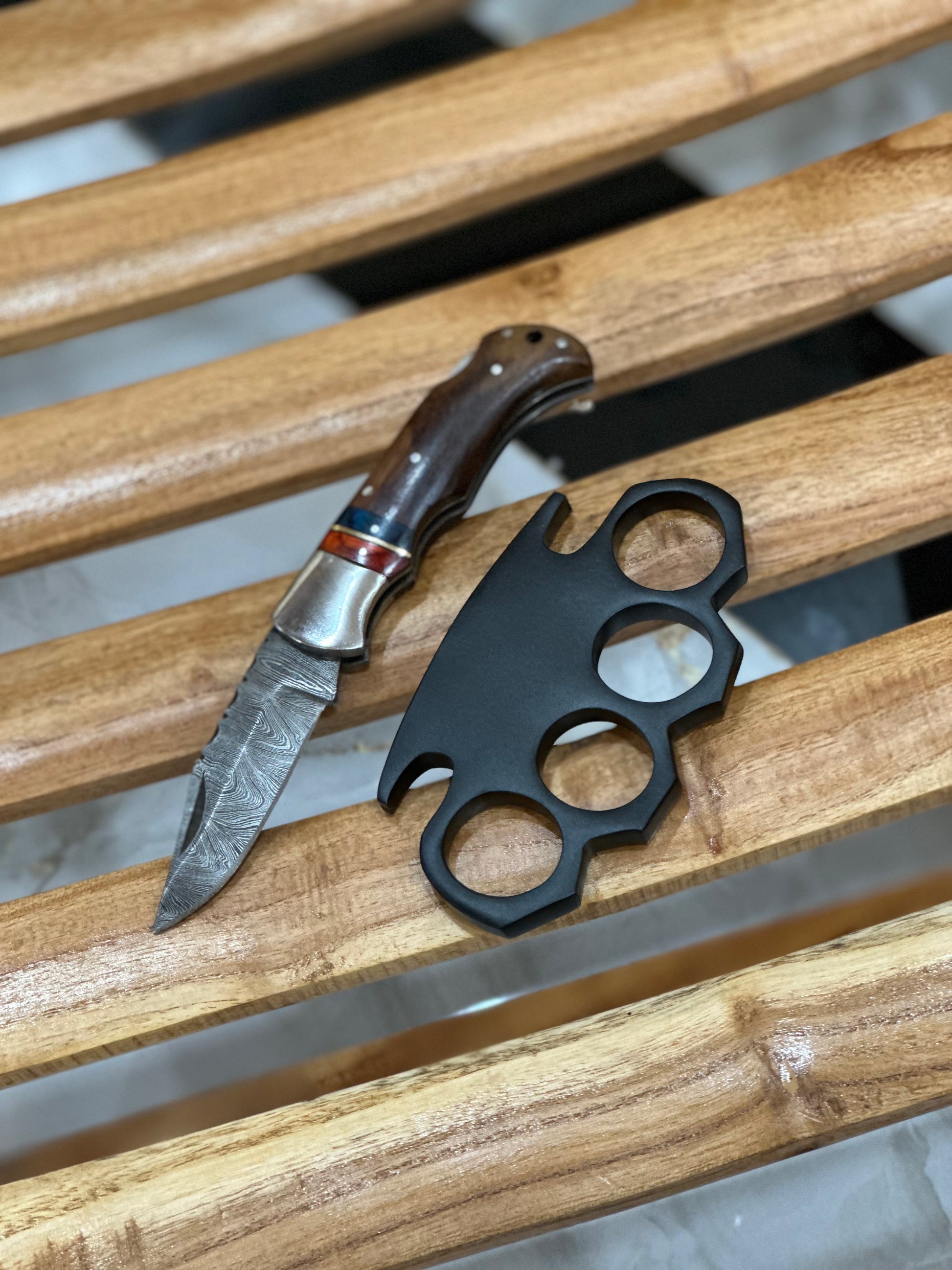Handcrafted black steel knuckle duster with integrated pocket knife and detailed engravings, paired with a leather case for self-defense