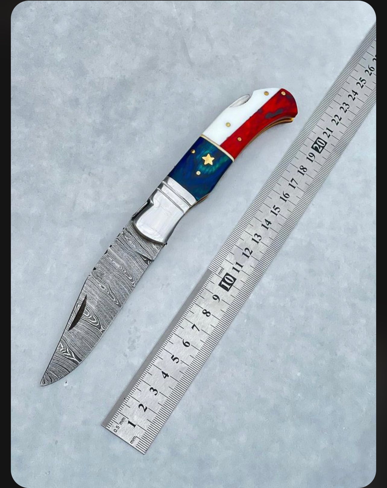 Compact Damascus folding knife with a 3-inch blade, American flag handle, steel bolster, and leather sheath for easy carry